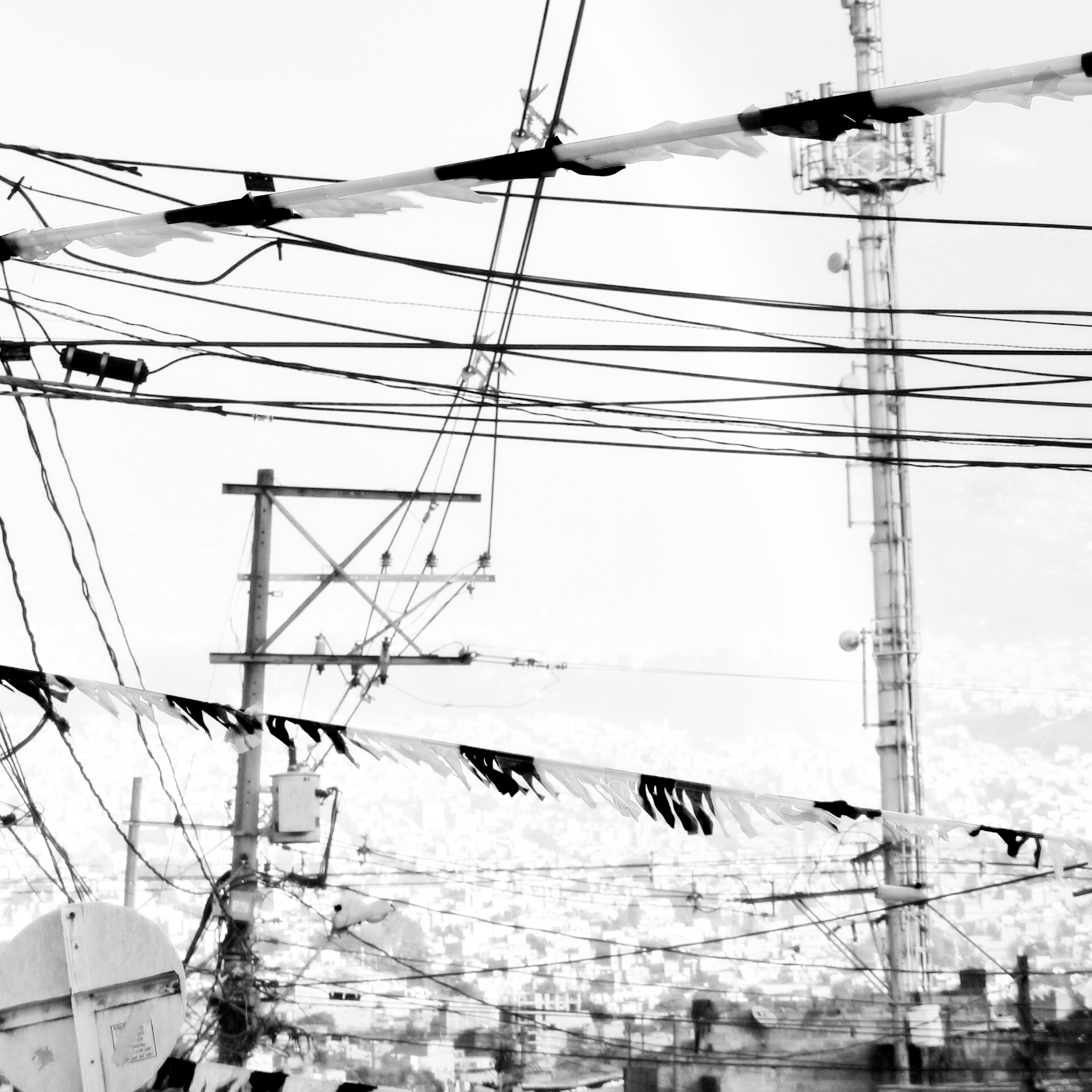 Fotografía en blanco y negro de un paisaje urbano de día, se ven postes de la electricidad, cables y banderines