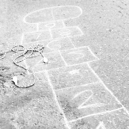 Fotografía en blanco y negro de una calle, se ve un gráfico de rayuela y un lazo para saltar